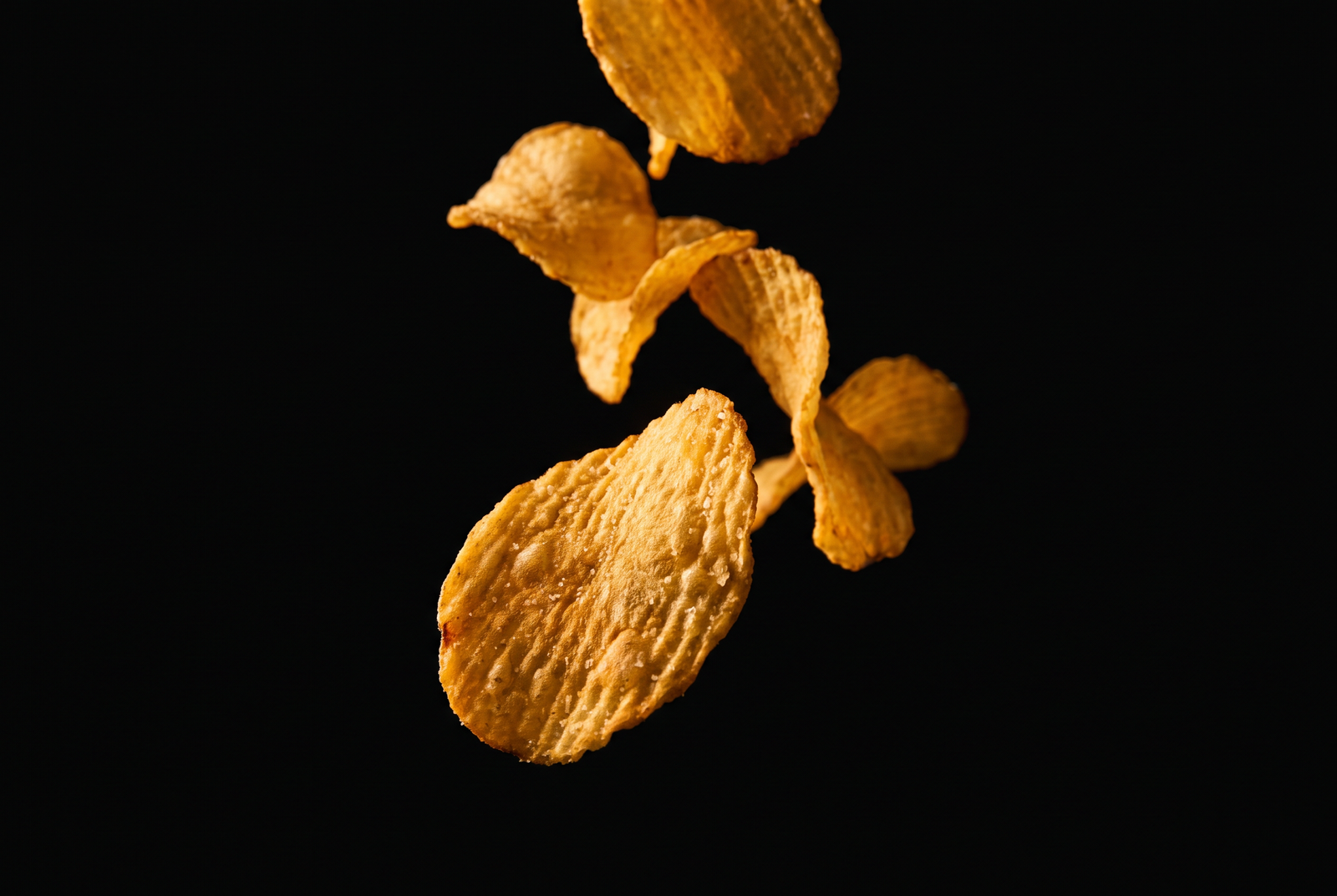Golden potato chips falling against a black background — Ghips chips fried in grass-fed ghee, never seed oils