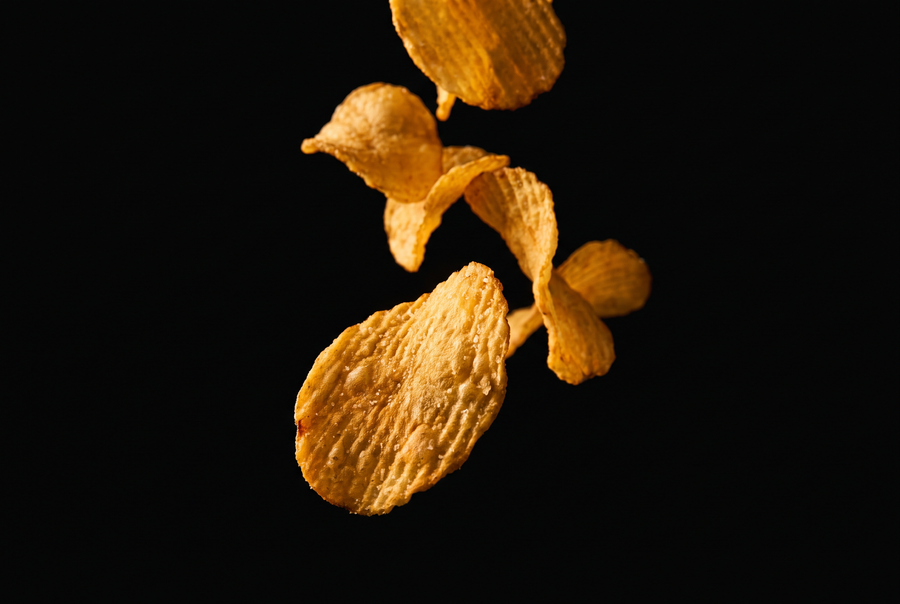 Golden potato chips falling against a black background — Ghips chips fried in grass-fed ghee, never seed oils