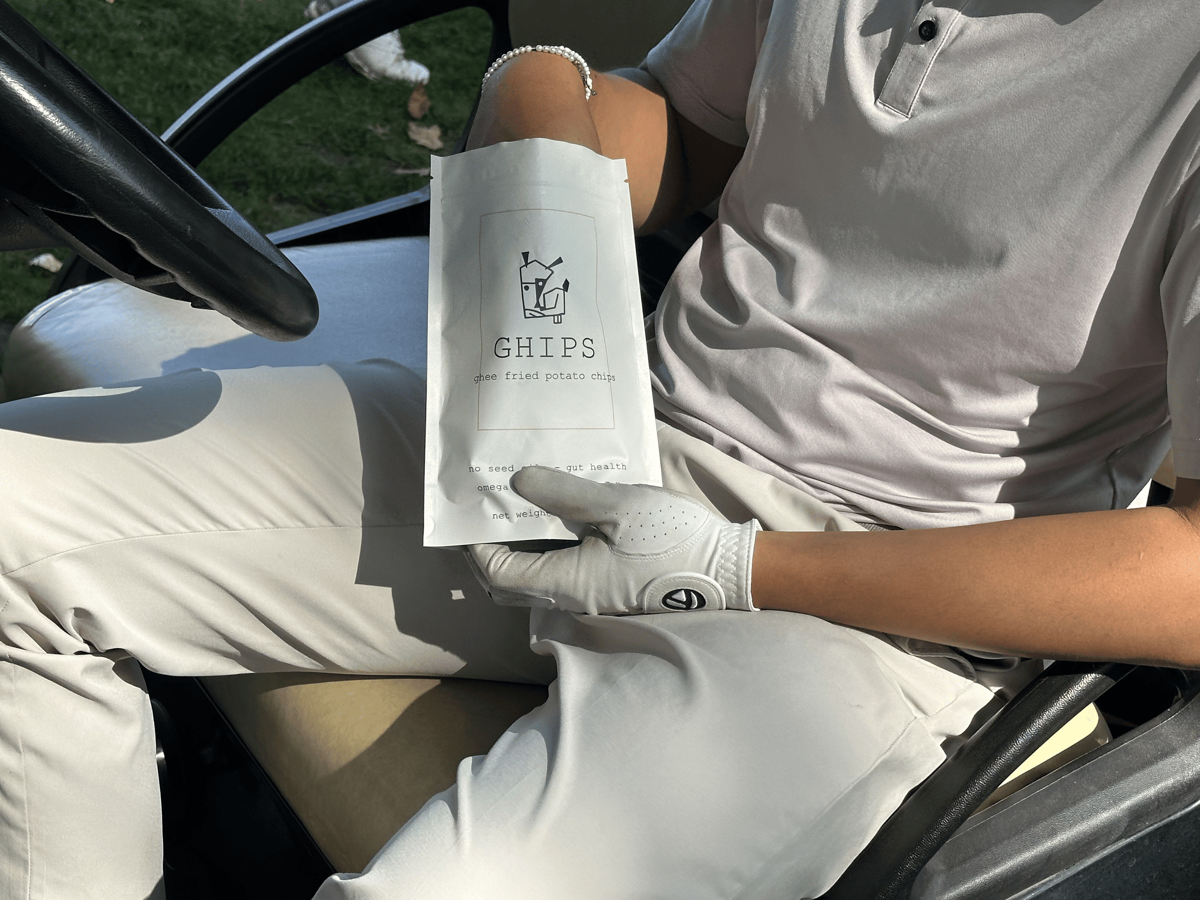Person sitting in a golf cart holding a white bag with 'GHIPS' branding.